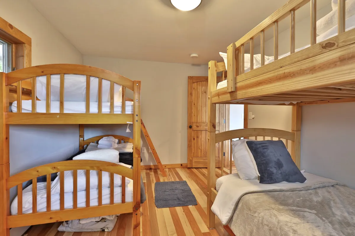 A cozy interior featuring bunk beds and a single bed, perfect for kids to unwind after a busy day. The warm wooden finishes and playful arrangement evoke the comfort of family sleepovers and rainy-day fun.