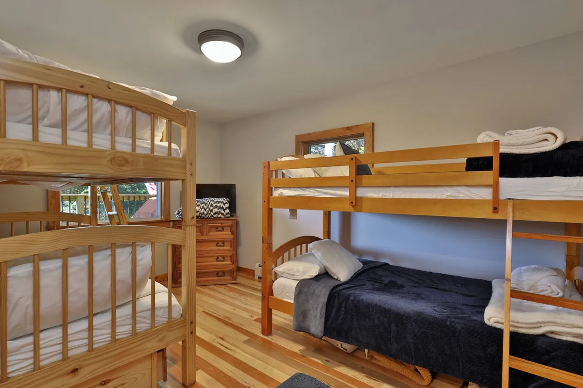 A playful bunk room featuring sturdy bunk beds, a dresser, and textured blankets. The space radiates warmth and fun, making it ideal for kids’ sleepovers, storytelling, and family bonding time.