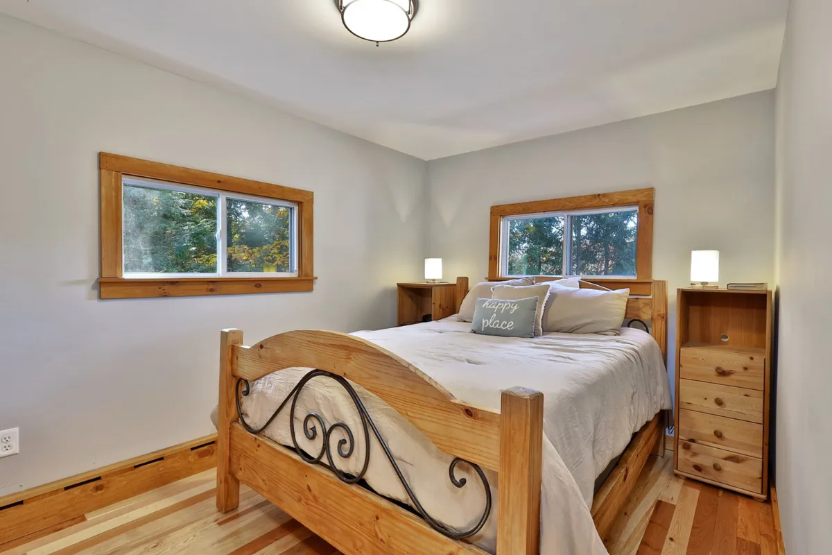 A queen bedroom featuring a wooden bed frame adorned with decorative pillows, bathed in natural light pouring through the windows. The serene setup is ideal for relaxation and restful nights after outdoor adventures.