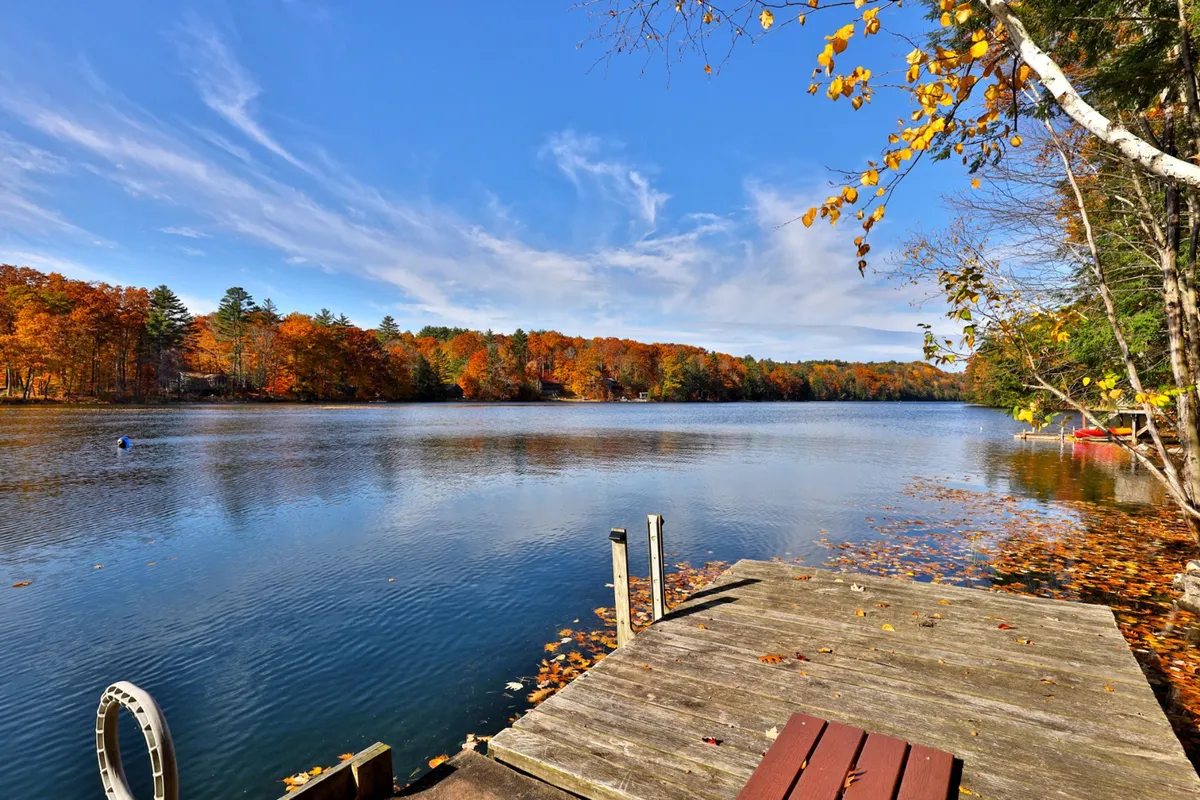 A tranquil lakeside scene featuring a calm lake surface, vibrant autumn foliage reflecting on the water, and a classic wooden dock extending out into the mist. The setting is bathed in soft natural light, evoking a sense of peaceful solitude and immersion in nature.
