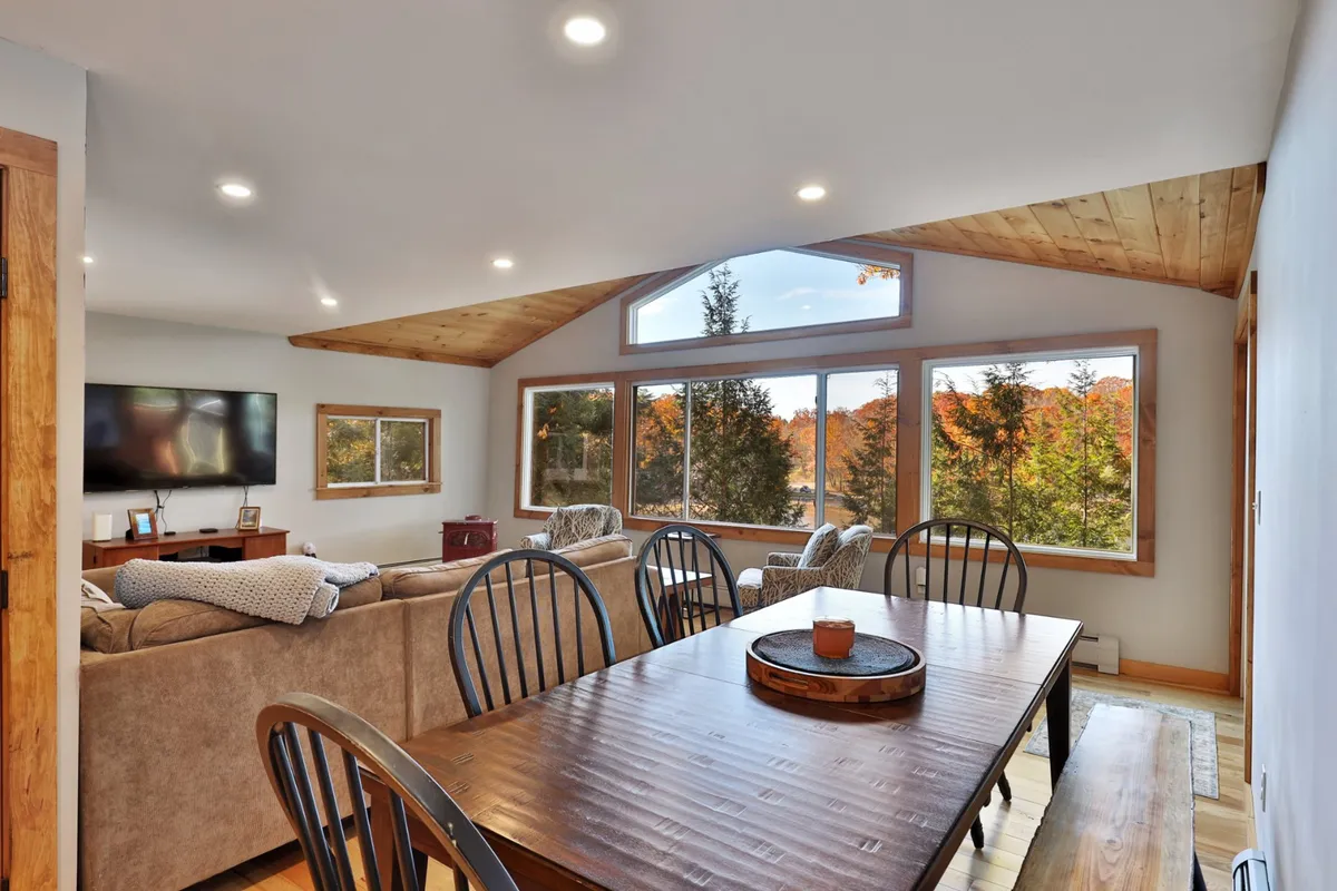 An inviting open-plan space that blends a dining table set with a centerpiece and a cozy seating area. Expansive windows overlook the landscape, allowing natural light to pour in and offering sweeping views—perfect for shared meals and memorable gatherings.
