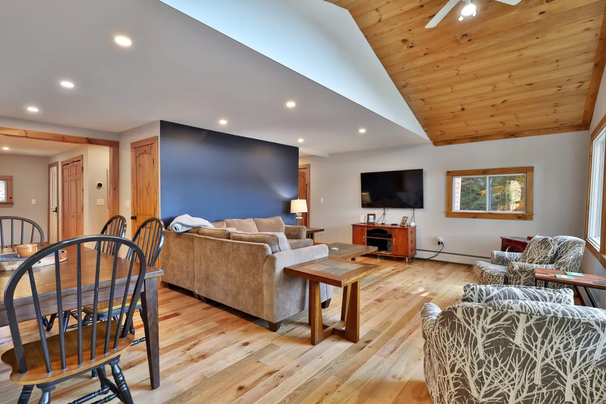 This image shows a cozy open-concept living and dining area featuring a comfortable sofa, a large dining table, a television prominently placed for easy viewing, and a big window letting in natural light. The space is inviting and perfectly set up for relaxing, dining, or gathering with family and friends, with clear visibility of the smart TV and areas suitable for Wi-Fi connectivity.