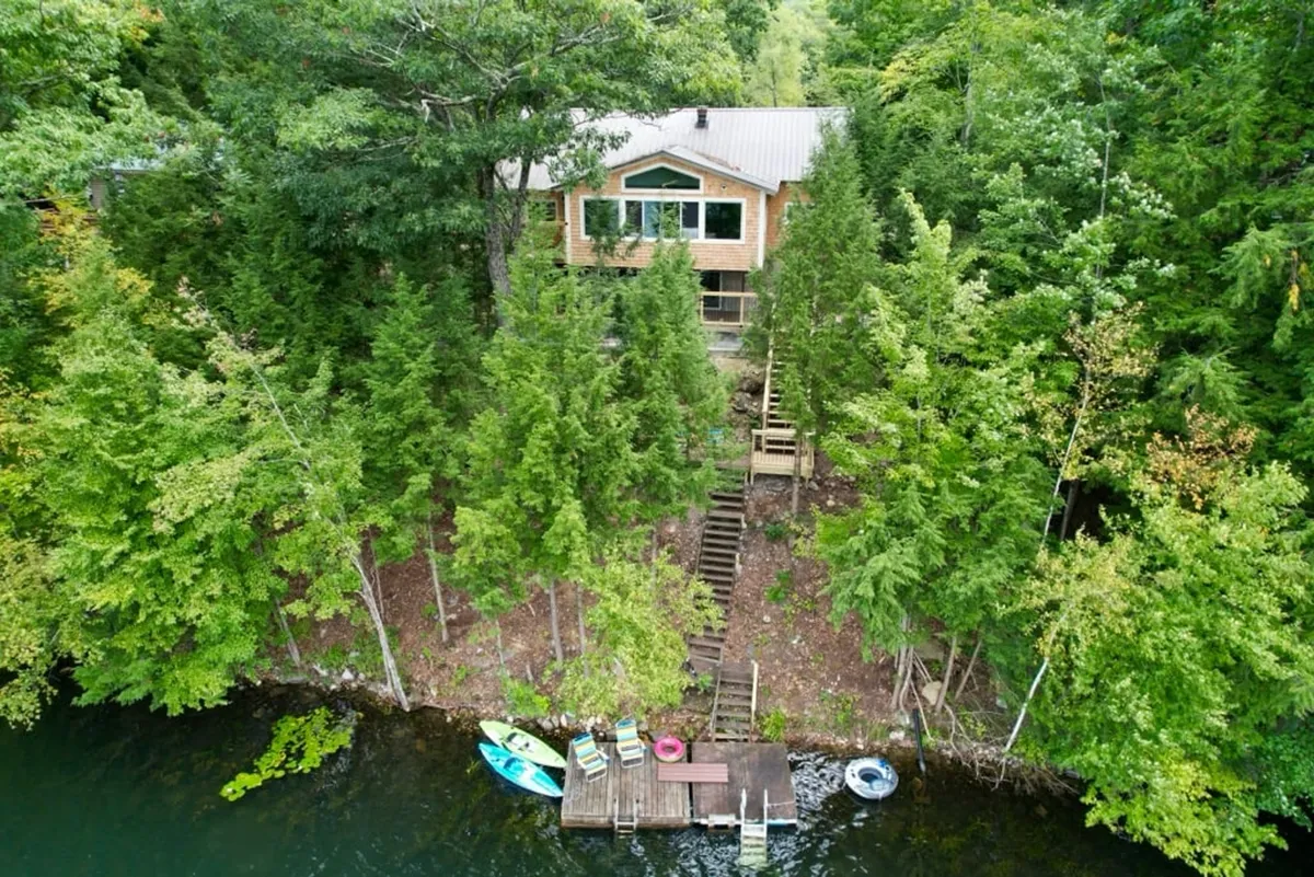This exterior shot captures the house with its private dock extending into Fern Lake and kayaks at the ready by the shoreline. The calm lake water, homey lodge, and accessible dock all feature prominently, with plenty of space for family fun and water activities.