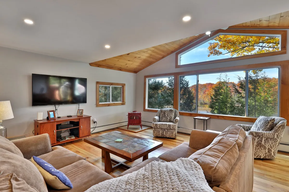 A spacious, sunlit living area featuring large windows with scenic lake views. The room includes a comfortable seating arrangement with plush sofas and a coffee table adorned with decorative elements, inviting guests to relax and connect while enjoying the tranquil backdrop of Fern Lake.