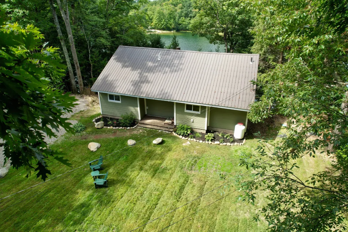 A wide exterior view featuring the house, a gently sloping lawn, and the shimmering lake beyond. The scene encapsulates the peaceful, secluded setting and the inviting openness of the property, framed by natural beauty.