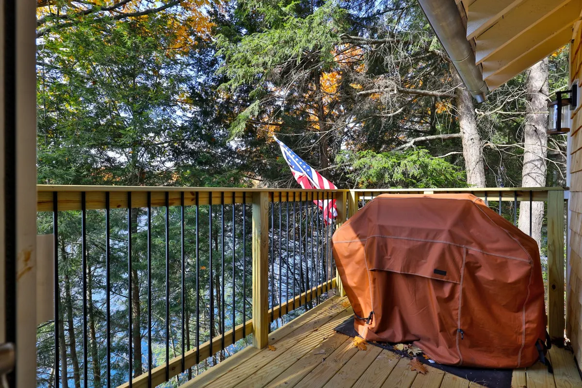 A tranquil exterior view of the wooden deck attached to the house, equipped with a grill and surrounded by trees. The deck looks out toward the lake and is ideal for outdoor dining and post-adventure relaxation, evoking summer barbecues and evenings under the stars.