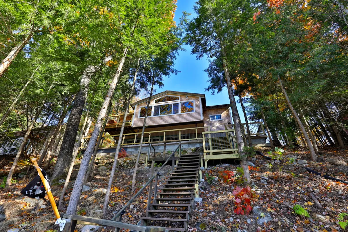 A view of the house framed by lush trees, with a wooden staircase leading down toward the landscape. The setting suggests proximity to nearby trails and a sense of immersion in nature—perfect for hikers, wildlife enthusiasts, or those seeking serene sunsets from the deck.